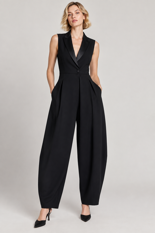 A woman modeling a sleeveless black jumpsuit with a structured collar, single front button, and wide-leg trousers, photographed against a plain light gray studio background.