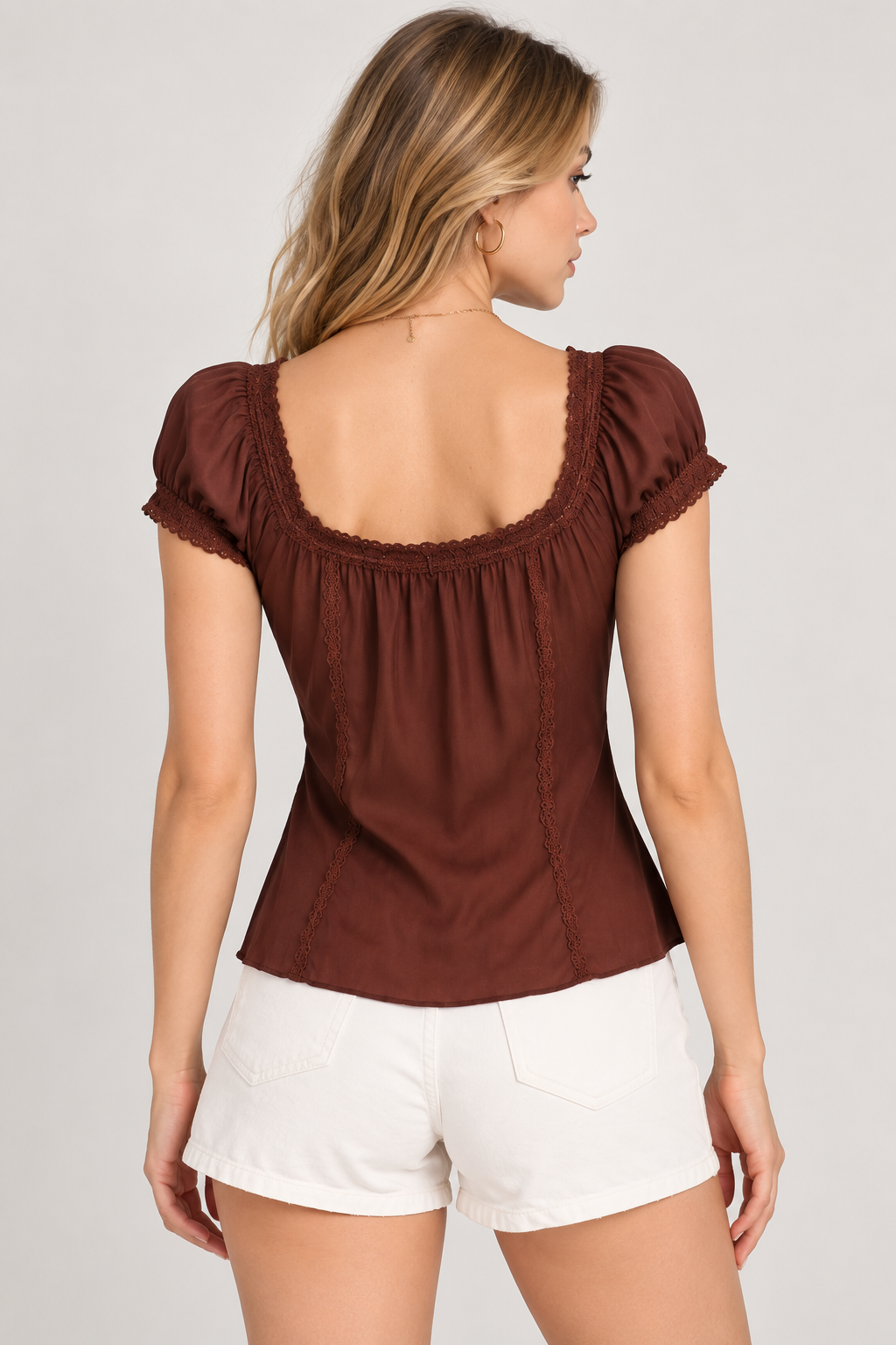 A woman shown from the back wearing a brown short-sleeve top with a square neckline, ruffled trim, and gathered waist, paired with white shorts, against a light gray studio background.