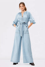 Light wash cotton denim palazzo jumpsuit with zip-front closure, wide-leg design, and belted waist by Nams-Ropa.