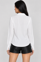 A woman shown from the back wearing a white long-sleeve button-up shirt and black faux-leather shorts against a light gray studio background.