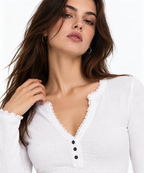 A close-up of a woman wearing a white long-sleeve top with a scalloped V-neckline and three black buttons, set against a plain white background.