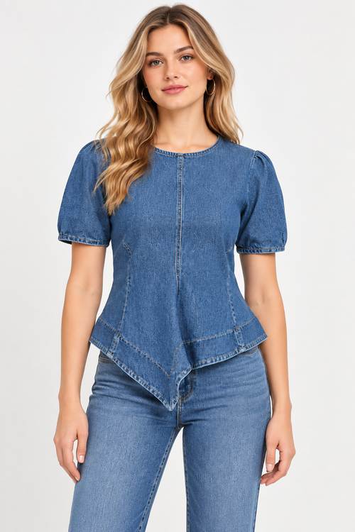 A woman modeling a blue denim short-sleeve top with puff sleeves and an asymmetrical ruffled hem, paired with blue jeans, against a plain light gray studio background.