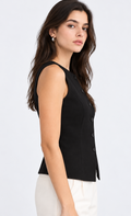 A woman shown in side profile wearing a sleeveless black vest with a buttoned front and white pants, photographed against a clean light gray studio background.