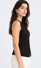 A woman shown in side profile wearing a sleeveless black vest with a buttoned front and white pants, photographed against a clean light gray studio background.